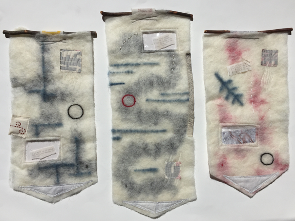 three felted collages hanging from sticks