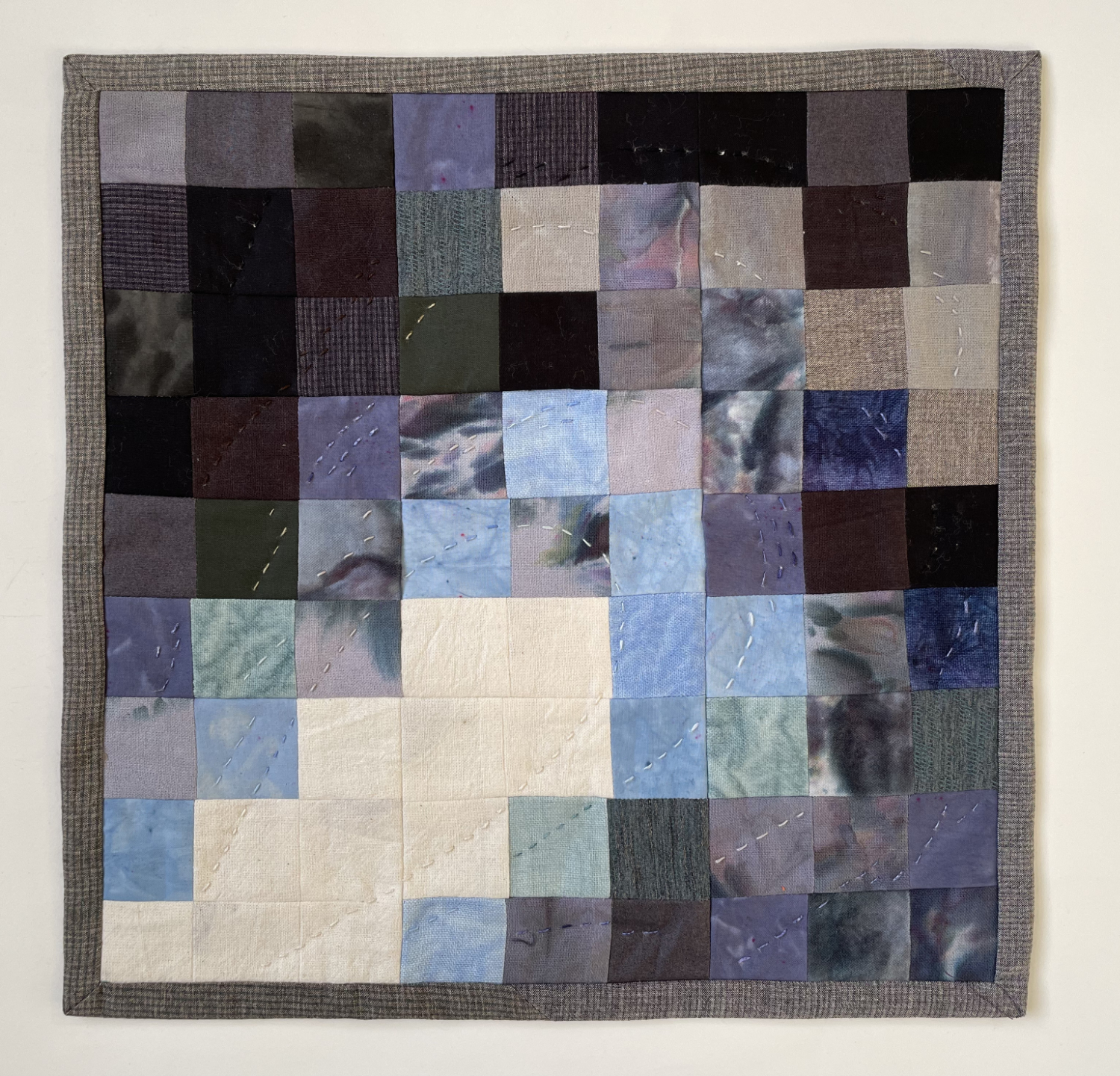 abstract pieced quilt with 9 x 9 squares with light on a diagonal pointing right and mussel shell colors around the edges 