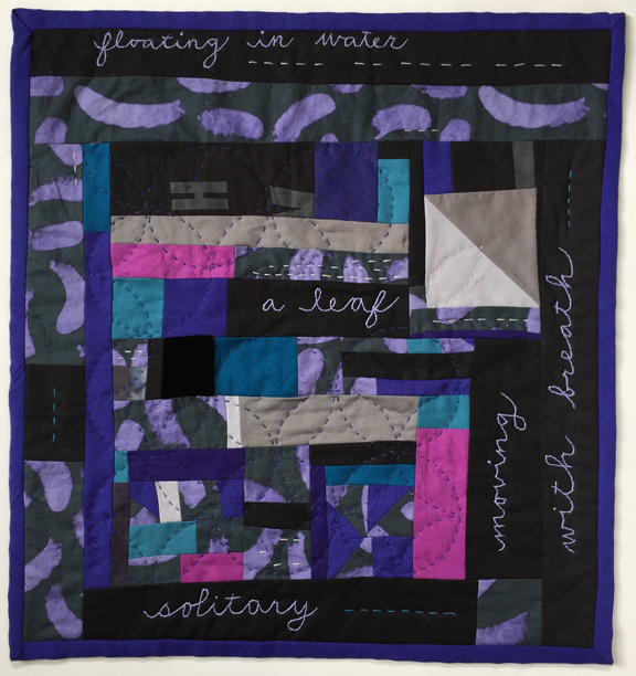 small randomly pieced quilt with embroidered text and sewn crossed circles with leaflike pattern