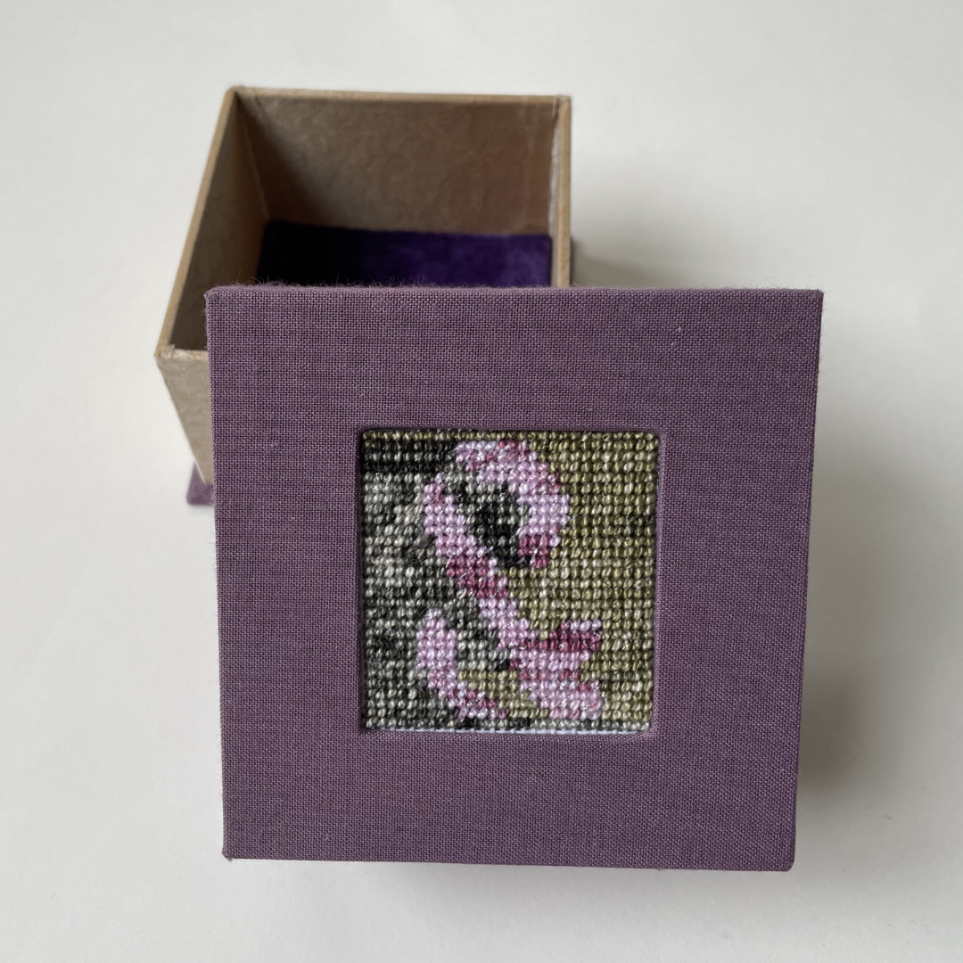 a box with a square needlepoint of an ampersand set in the cover