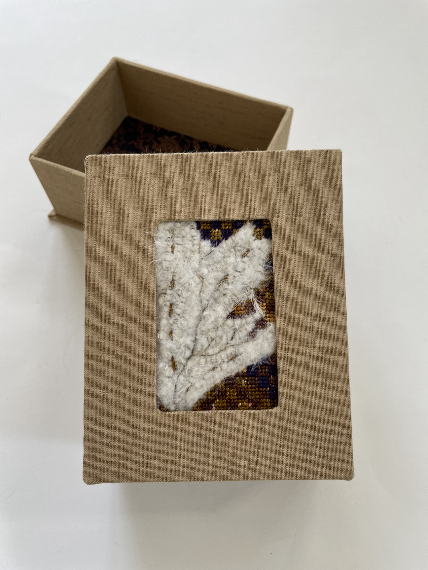 a box with an inset needlepoint of feathers on checkerboard background