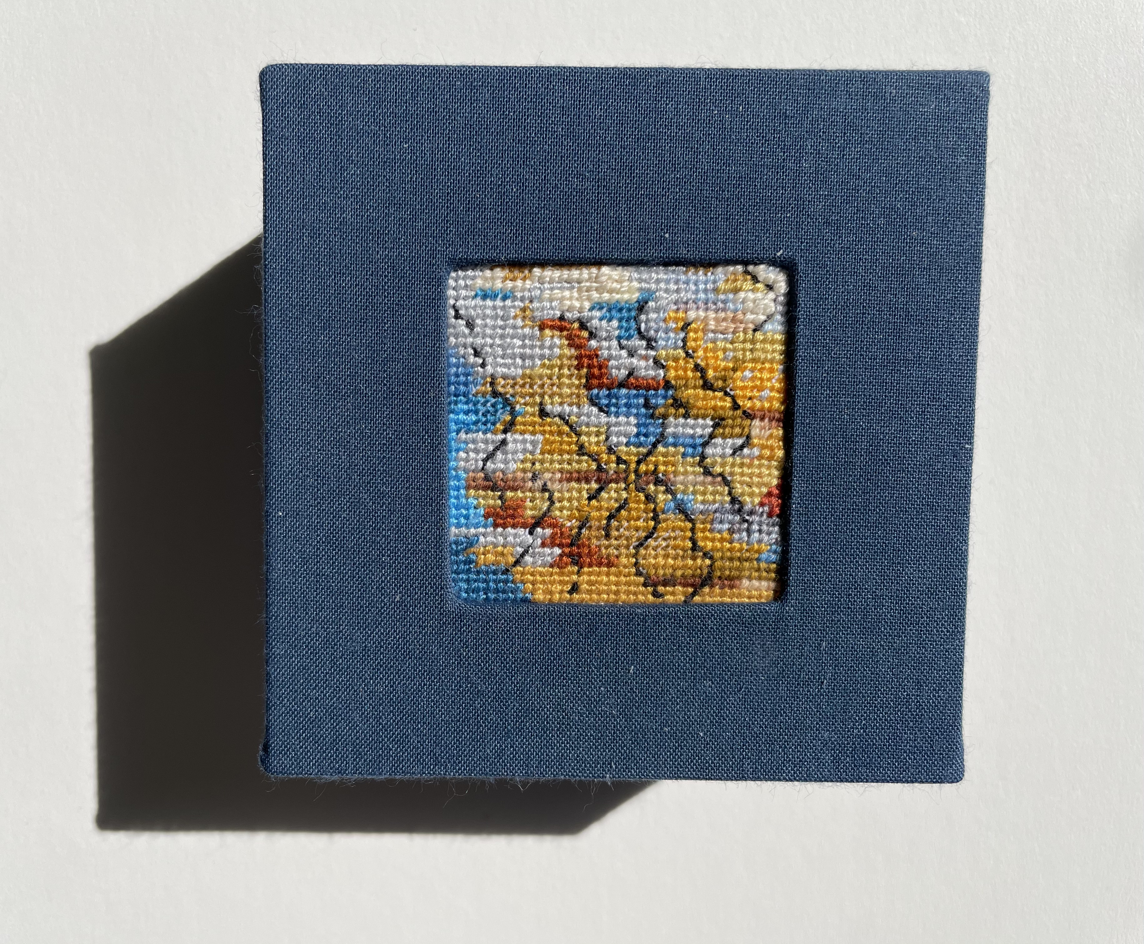 a box with an inset needlepoint of wavy lines on land and sea colored background