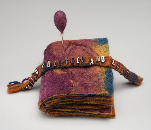 felted book with faces stitched on the pages and large needle stuck through it